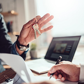 A Hand Holding Keys and Someone Signing a Document